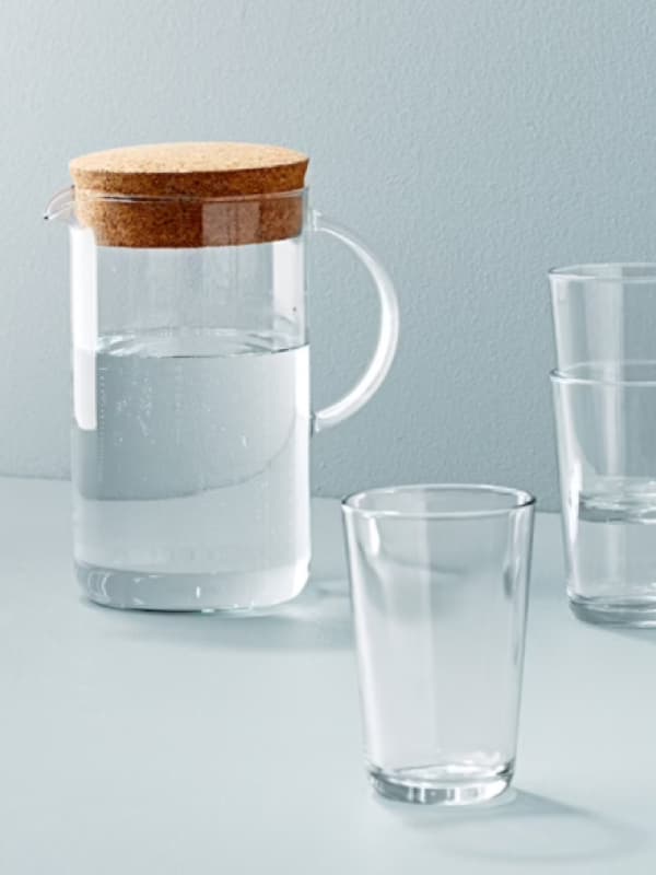 Una caraffa in vetro trasparente con coperchio in sughero e vicino dei bicchieri.