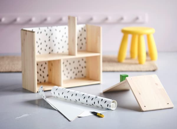 Una casa de nines IKEA FLISAT en procés de muntatge i decoració per utilitzar d’emmagatzematge per als nens al passadís.