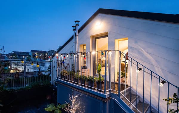 Una casa vista da fuori, con la facciata con tetto a punta e il balconcino. Dentro le luci sono accese e si sente atmosfera di casa. La porta è aperta.
