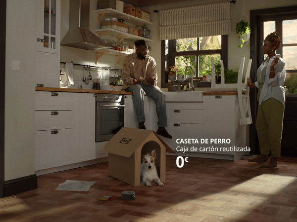 Una caseta de gos amb un gos dins, en una cuina on dues persones estan parlant.