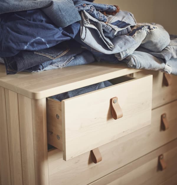 Una cassettiera BJÖRKSNÄS in legno massiccio. Un cassetto è leggermente aperto. Sopra, una serie di tessuti in jeans.