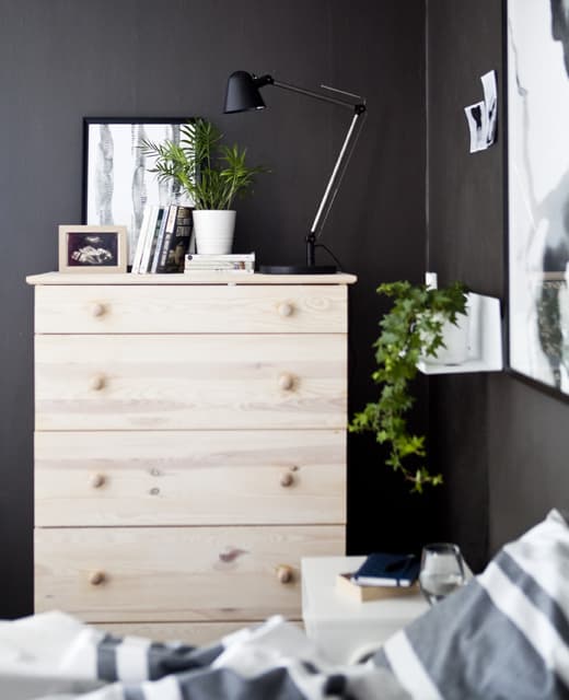 Una cassettiera di legno chiaro in una camera da letto grigio scuro.
