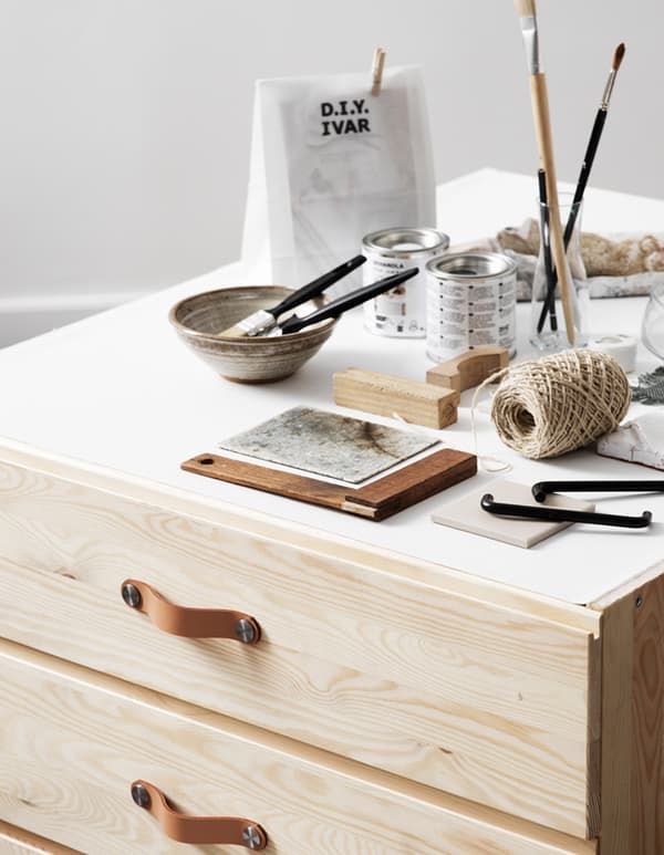 Una cassettiera IVAR con tre cassetti con sopra pennelli, un busta di carta, un gomitolo di spago e altri oggetti per personalizzare il mobile.