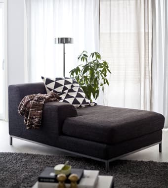 Una chaise longue grigio scuro in un soggiorno monocromatico.