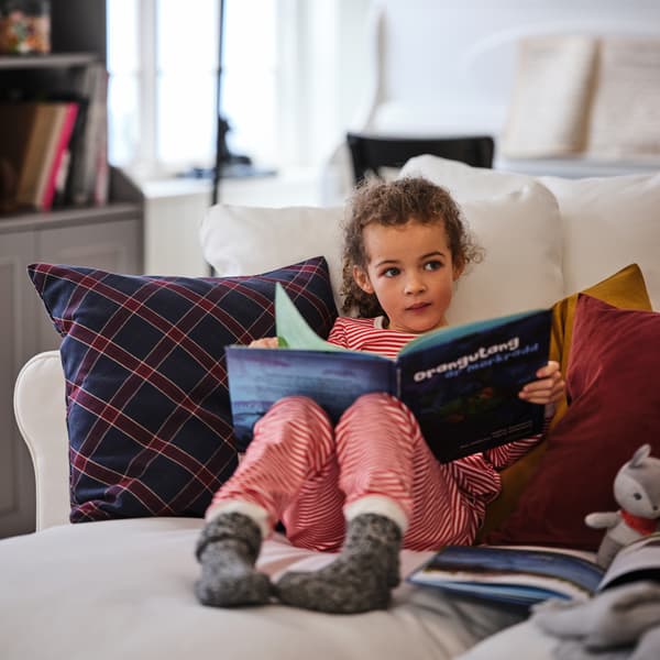 Una chica en pijama, cómodamente sentada con un libro en un sofá GRÖNLID blanco de cuatro asientos con chaise longue
