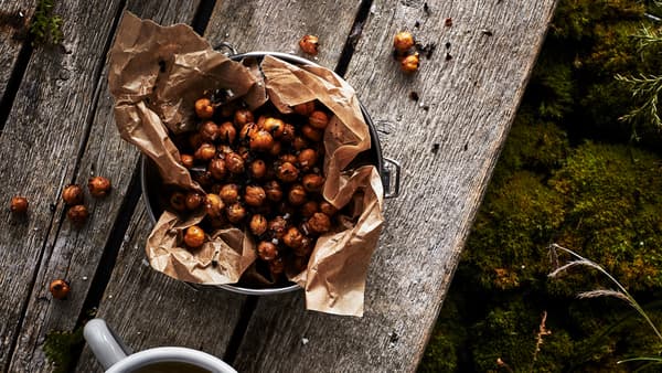 Una ciotola rivestita con carta da forno, su un tavolo rustico in legno, piena di ceci tostati con tè chai e peperoncino. Accanto, una tazza - IKEA
