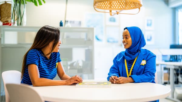 Una co-worker IKEA in uniforme scende le scale di un negozio IKEA per salutare dei clienti, portando una borsa