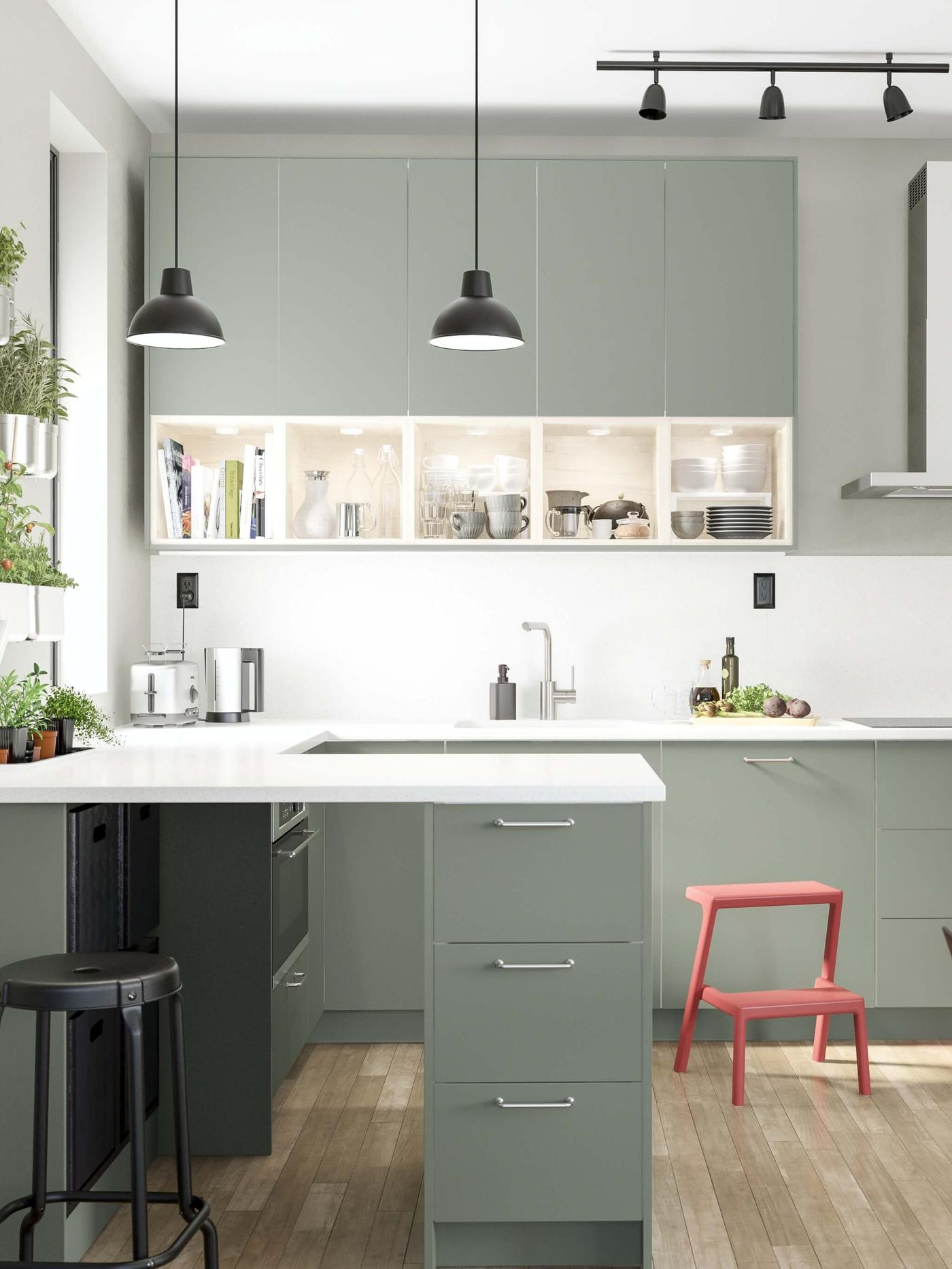 Una cocina BODARP verde grisáceo con dos pantallas colgantes y un taburete rojo en el suelo.