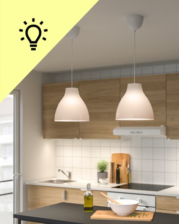 Una cocina con dos lámparas de techo encendidas y en la esquina superior izquierda de la foto un triángulo amarillo con un ícono de ampolleta.