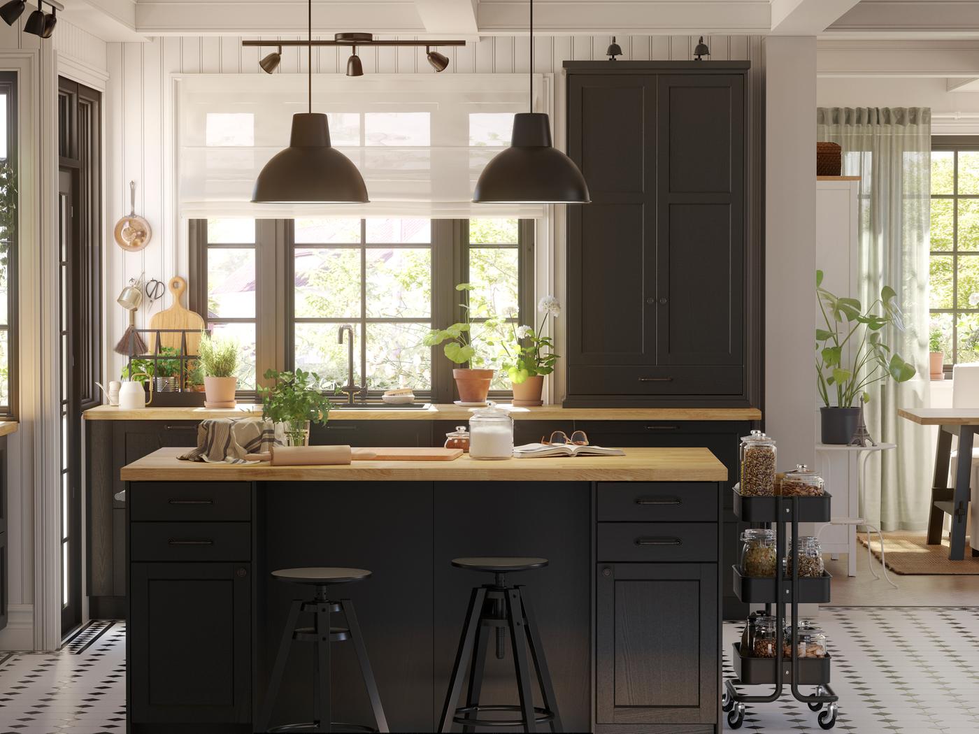 Una cocina LERHYTTAN grande con frentes pintados de negro y una isla de cocina en el centro con dos lámparas de techo negras encima.