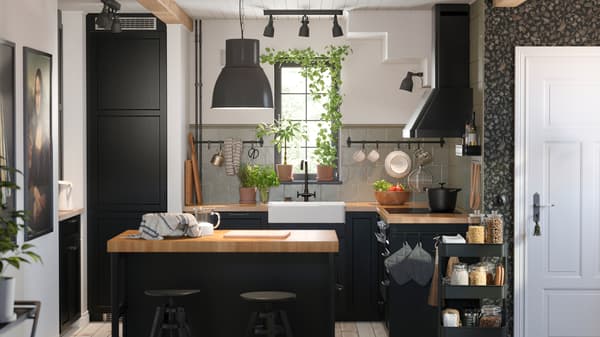 Una cocina pequeña con frentes acabados en negro LERHYTTAN con una encimera de madera y una isla de cocina con una lámpara colgante negra.