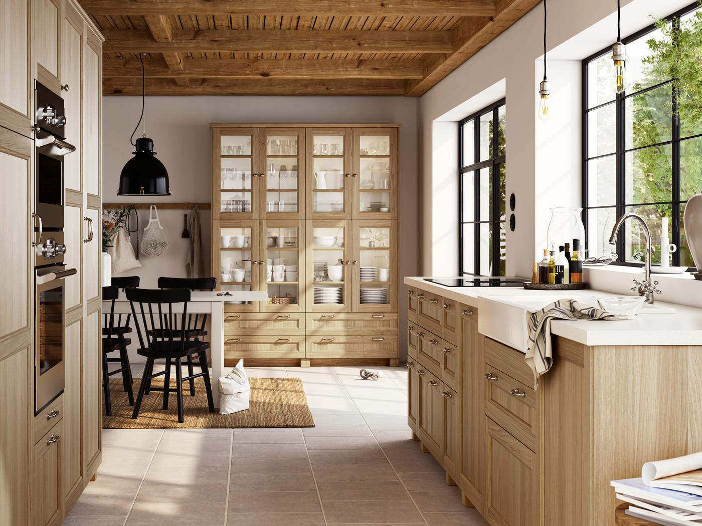 Una cocina rústica con frentes de efecto roble VEDHAMN, armarios de cocina, una mesa con varias sillas y un fregadero HAVSEN en blanco.