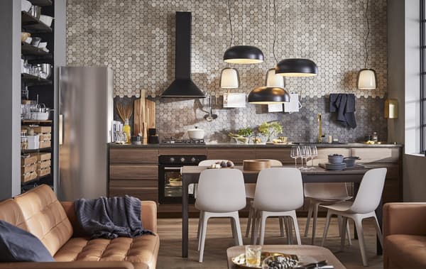 Una cocina, salón, comedor de plano abierto con sofás de piel marrón y armarios de cocina de madera oscura delante de una pared alicatada.