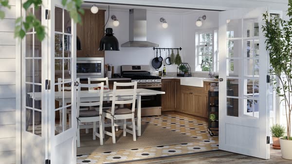 Una cocina soleada con puertas ENKÖPING efecto nogal en los gabinetes y una mesa blanca con algunas sillas a su alrededor.