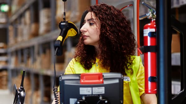 Una col·laboradora d'IKEA amb els cabells llargs i foscos condueix un carretó elevador a l'àrea d'autoservei.