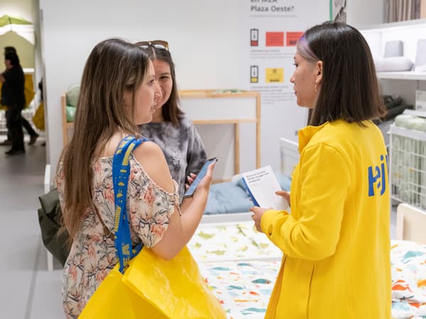 Una colaboradoras IKEA con uniforme amarillo hablando con dos clientas. Una de las clientas tiene una bolsa de compras IKEA colgada al hombro