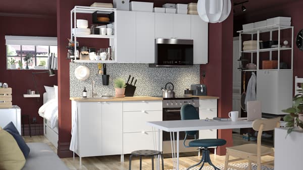 Una combinación de cocina ENHET blanca a lo largo de una pared en un departamento tipo estudio con un escritorio al frente y una cama detrás de la pared.