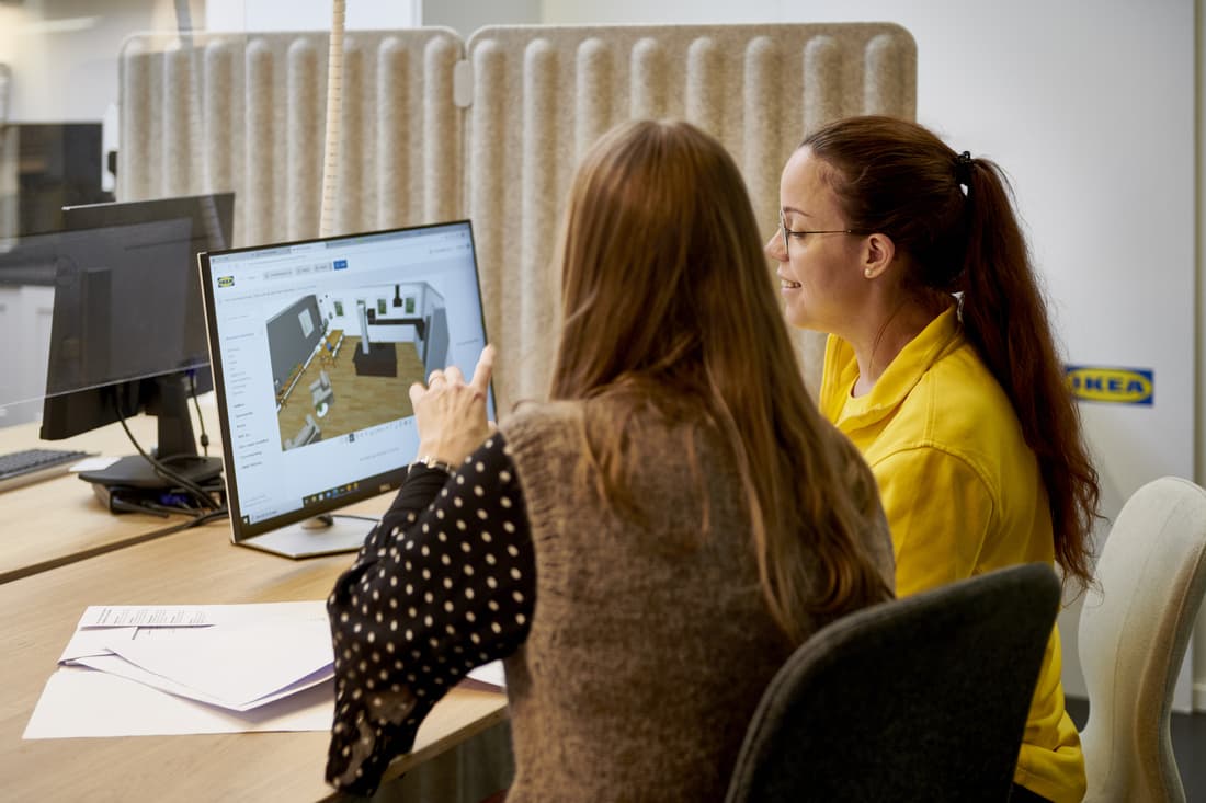 Una coworker IKEA in divisa e una cliente stanno progettando una cucina insieme alla scrivania.