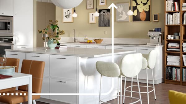 Una cucina bianca con isola a vista e due sgabelli in tessuto bianco. Sulla sinistra si intravede un tavolo da pranzo con sedie in pelle marrone. 
