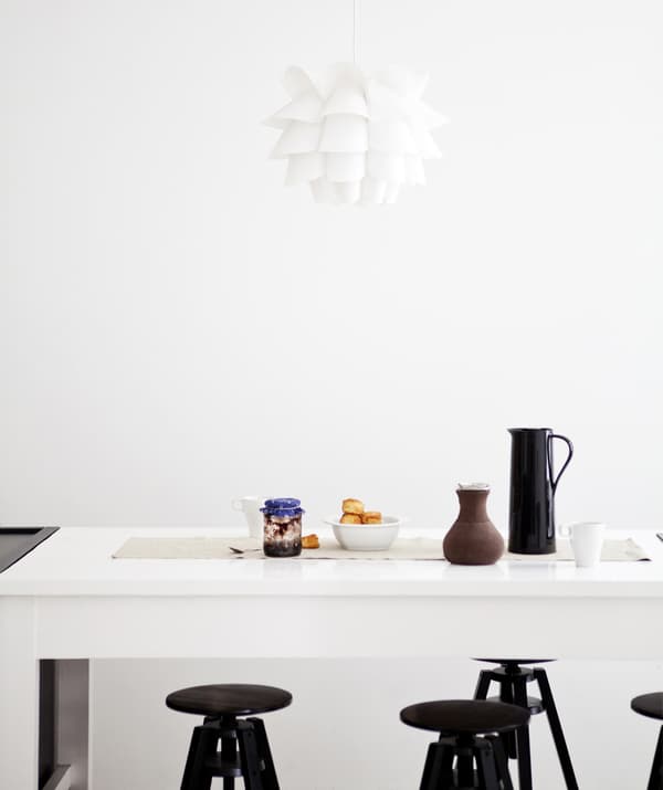 Una cucina bianca con un piano di lavoro, sgabelli neri e una lampada a sospensione bianca.