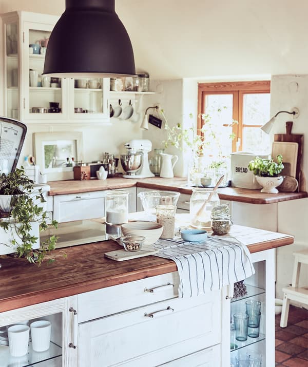 Una cucina bianca in stile rustico con piani di lavoro in legno e alcuni ingredienti di una ricetta disposti sull'isola.
