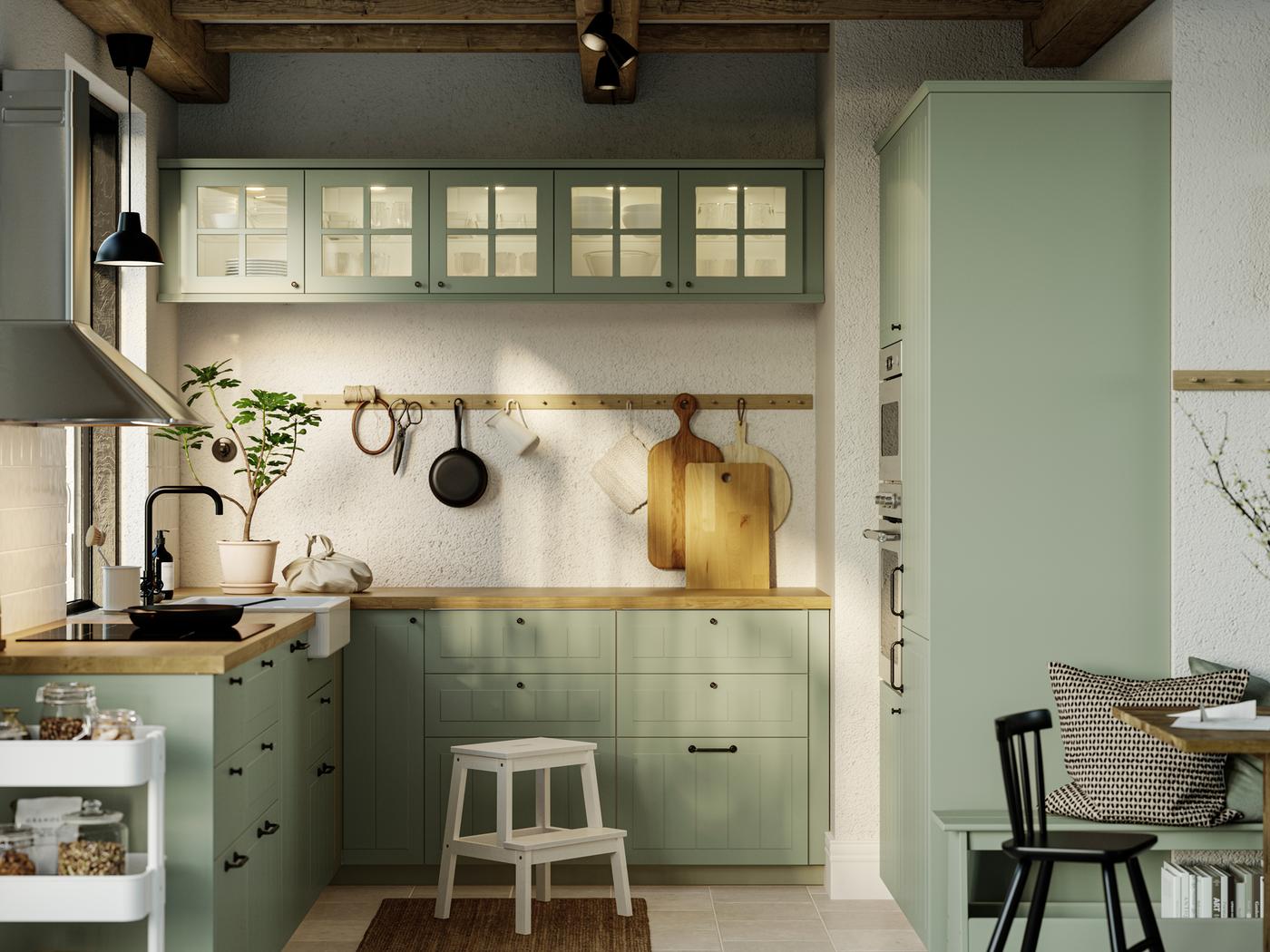 Una cucina con frontali STENSUND verde chiaro, un piano cottura a induzione GRUNDAD nero e una cappa installata a parete MATTRADITION - IKEA.