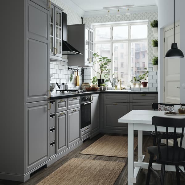 Una cucina con mobili grigi illuminata da un'ampia finestra. Accanto, un tavolo bianco e sedie nere.