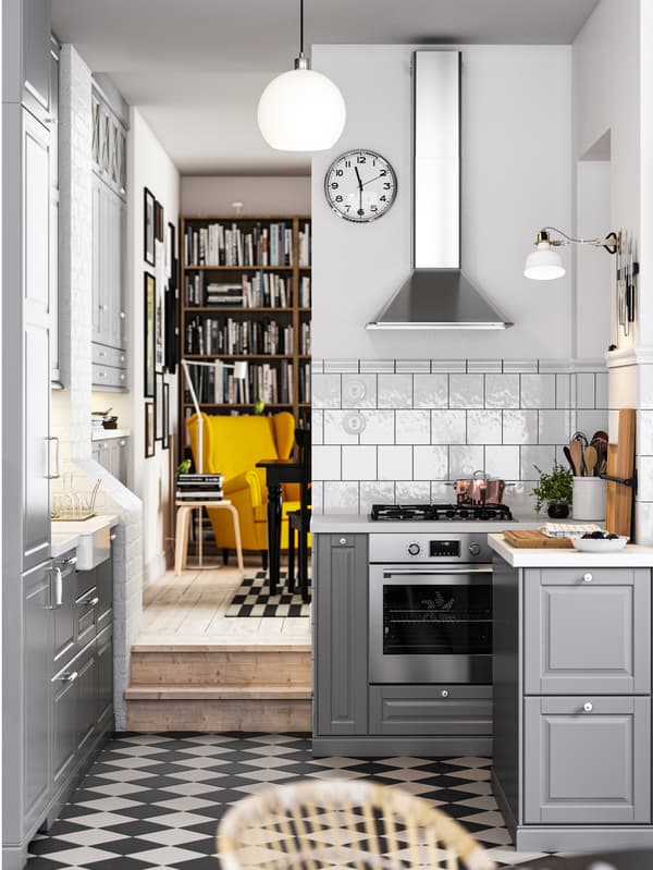 Una cucina in stile tradizionale con pavimento a scacchiera, frontali per cucina BODBYN grigi e piani di lavoro bianco/grigio chiaro effetto pietra/laminato.