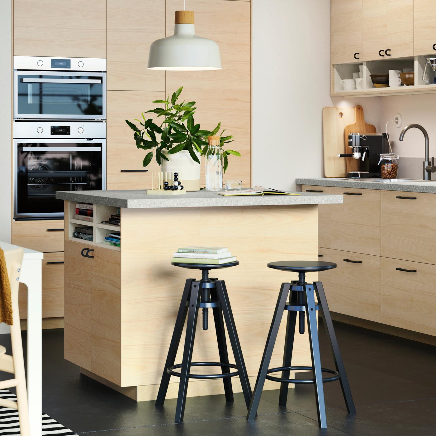 Una cucina luminosa con pavimento scuro, frontali FRÖJERED in bambù chiaro, un'ampia isola per cucina e due sgabelli neri.