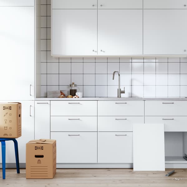Una cucina METOD bianca nelle fasi finali del montaggio. Un cassetto è sul pavimento e il suo frontale è appoggiato a un mobile.
