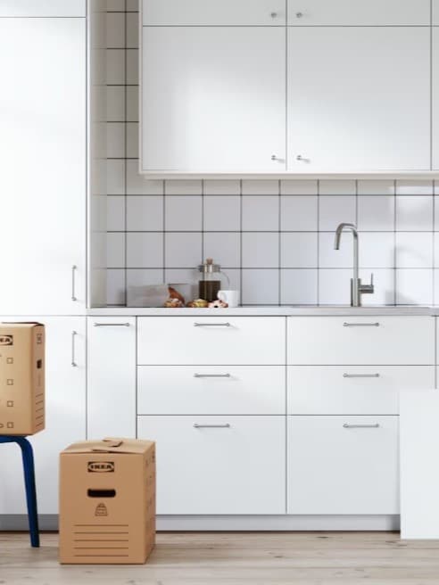 Una cucina METOD bianca nelle ultime fasi di installazione. Ci sono due scatoloni di cui uno su uno sgabello MARIUS.