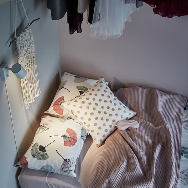 Una cuscino SKÄGGÖRT su un divano letto illuminato da una lampada da parete.