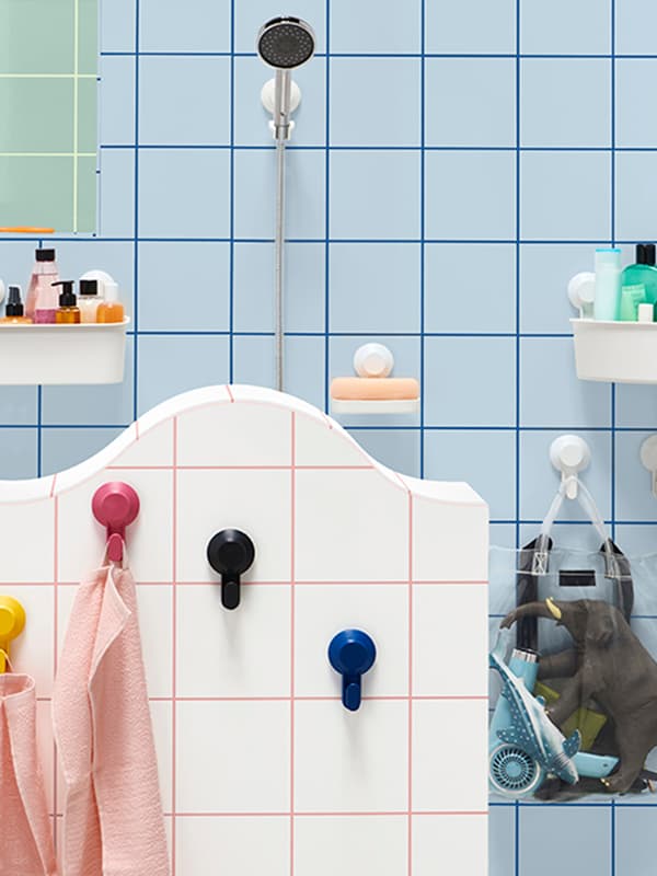 Una doccia a muro con davanti una parete con ganci a ventosa colorati cui sono appesi asciugamani. Nella stanza, ci sono anche altri ganci con una borsa trasparente e alcuni supporti a parete a ventosa contenenti oggetti.