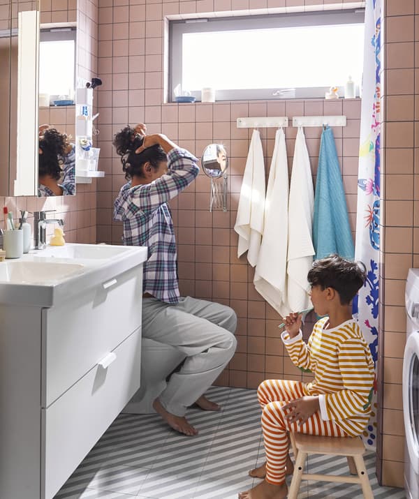 Una dona adulta i un nen en una cambra de bany amb lavabo de dos piques, un tamboret i dos miralls.