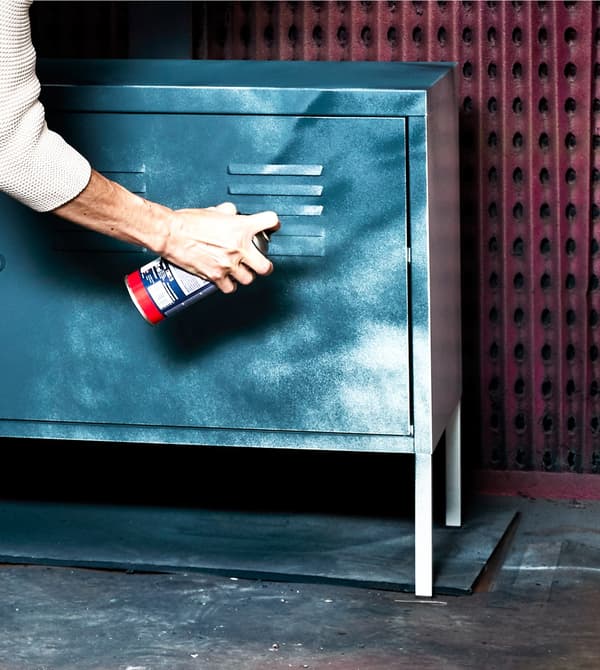 Una dona pinta amb esprai blau un armari IKEA PS blanc per aportar una nova imatge.