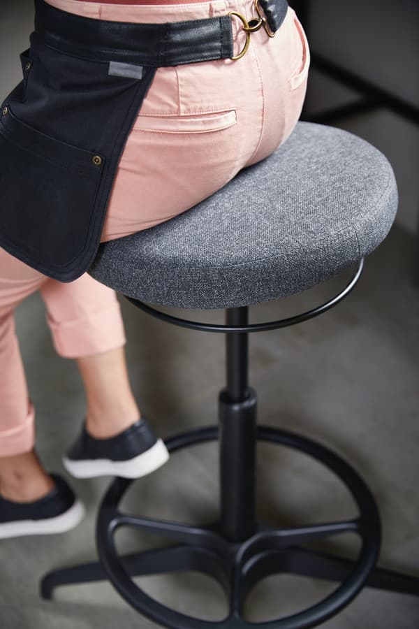 Una donna con dei pantaloni rosa siede su uno sgabello per seduta attiva LIDKULLEN grigio.