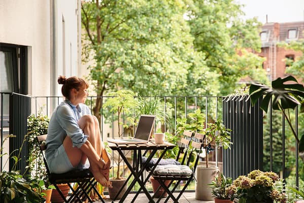 Una donna è seduta su una sedia sul suo balcone con un portatile aperto sul tavolo.