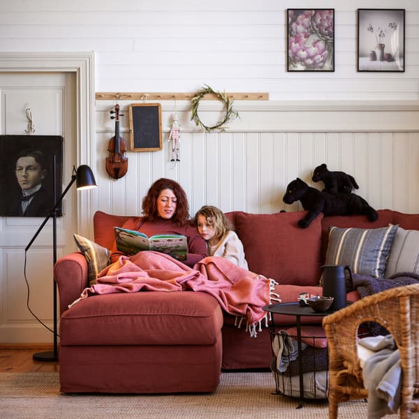 Una donna e una bambina sedute su un divano GRÖNLID con chaise longue rosso chiaro, accanto a una lampada da terra nera e un tavolo/contenitore nero.