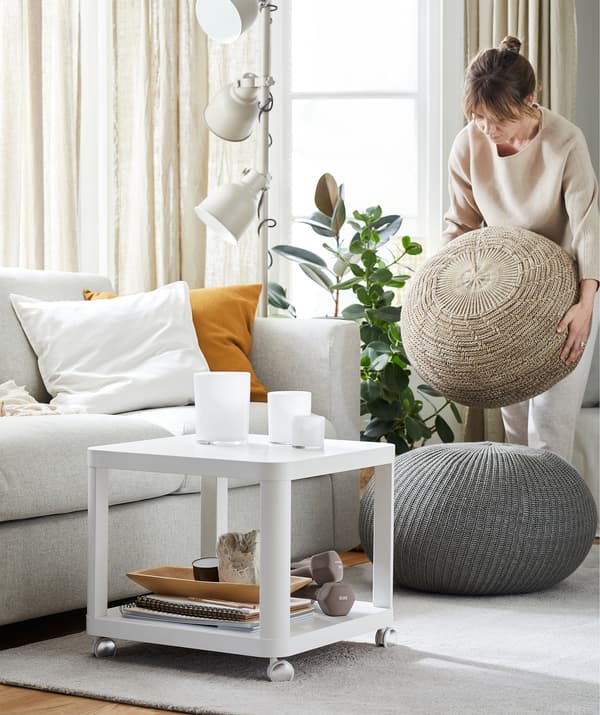Una donna in soggiorno con un divano, un tavolino con rotelle, un tappeto e un pouf rotondo che sta spostando - IKEA