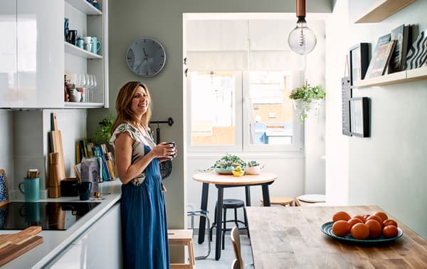 Una donna in una cucina in stile cambusa con ante bianche, un tavolo bar in legno e una piccola zona pranzo in fondo - IKEA