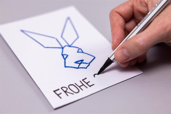 Una donna infila un filo in un foglio di carta e scrive su un bigliettino «Buona Pasqua»