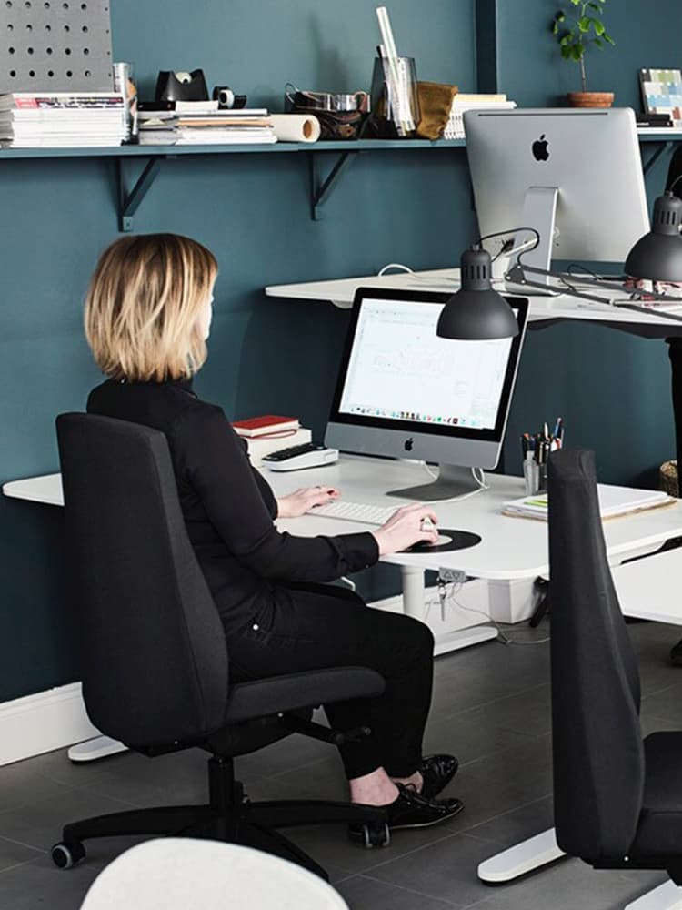 Una donna lavora in ufficio sulla sua scrivania osservando il suo pc. Sulla scrivania ci sono mouse, tastiera ed dei libri. 