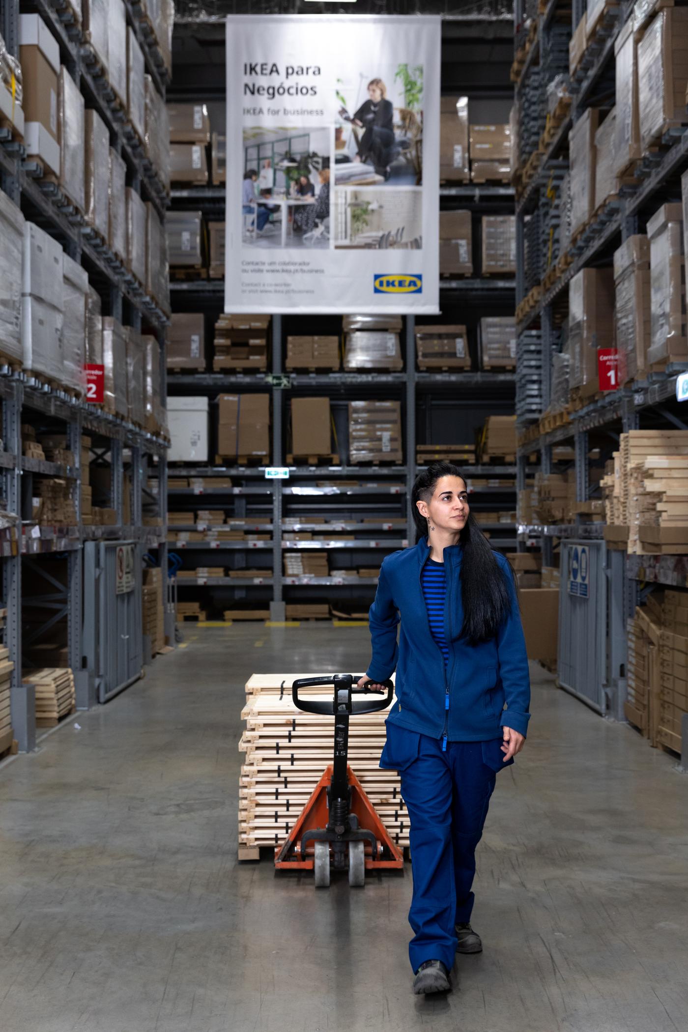 Una donna nel magazzino IKEA mentre sta trasporando diverse scatole con un carrello.