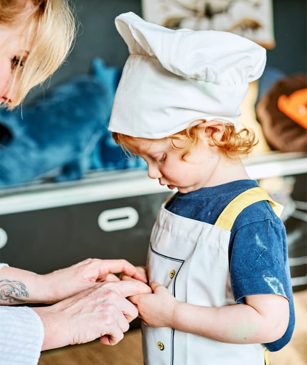 Una donna prende le mani di un bambino vestito da chef.