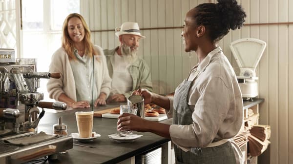 Una donna serve il caffè a due persone al bancone di un'accogliente caffetteria.