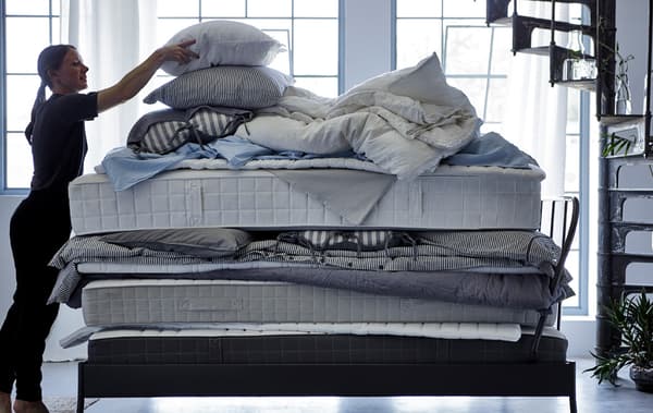 Una donna sistema un cuscino in cima a una catasta di materassi, piumini e biancheria da letto - IKEA