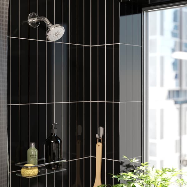 Una ducha con cerámica negra  donde se ven colgadores de pared con artículos de baño. Arriba una ducha IKEA.