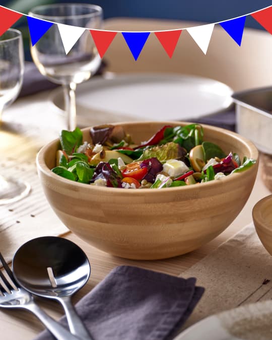 Una ensaladera de madera con ensalada sobre una mesa.