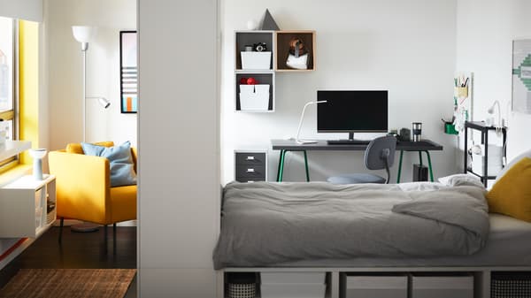 Una estructura de cama PLATSA con almacenaje en una habitación con un sillón y una silla giratoria gris delante de un escritorio con caballetes verdes.
