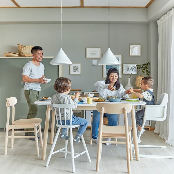 Una famiglia in una zona pranzo. La madre e i due figli sono seduti a tavola, mentre il padre si avvicina con una ciotola - IKEA